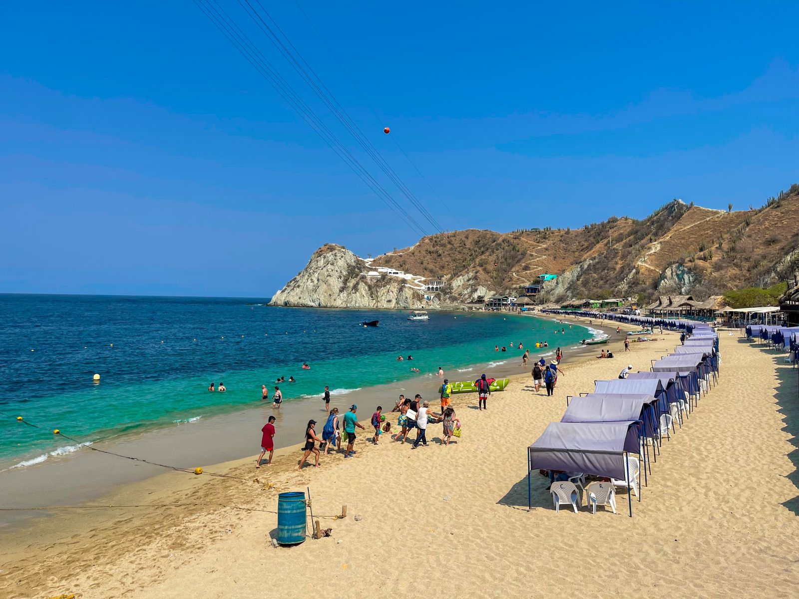 Playa Blanca: fila de carpas de sombra sobre arena clara junto a mar turquesa con montañas al fondo